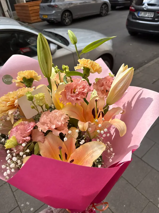 Strauß mit pfirsichfarbenen Lilien, Nelken und Lisianthus in pinkem Papier