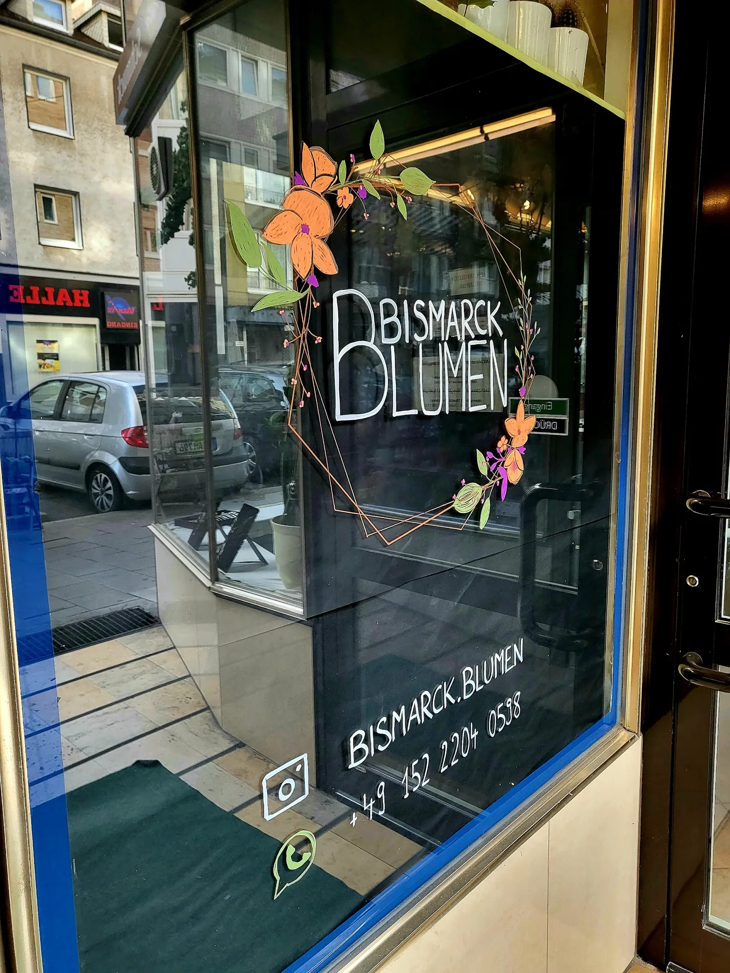 Schaufenster mit dem handgezeichneten Bismarck-Blumen-Schriftzug und orangefarbenen Blüten